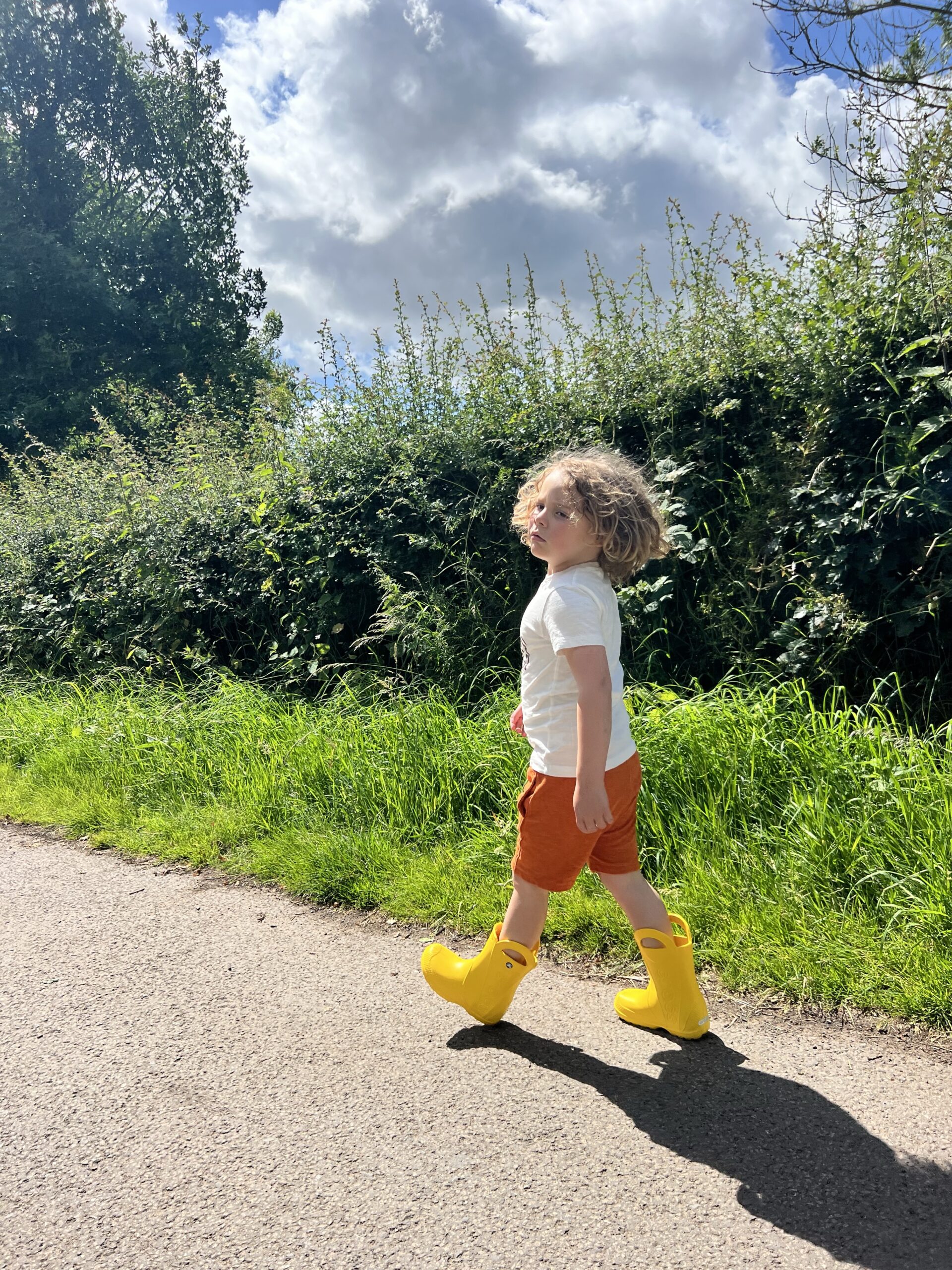A child wearing yellow rain boots walking down a road.