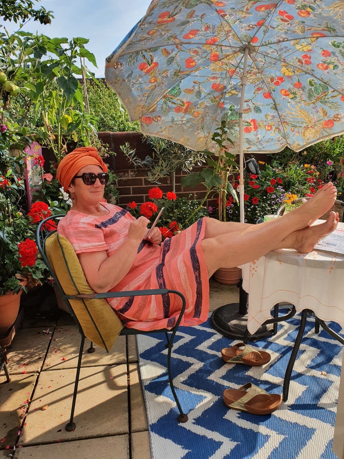 A woman sitting in a chair on a patio under an umbrella.