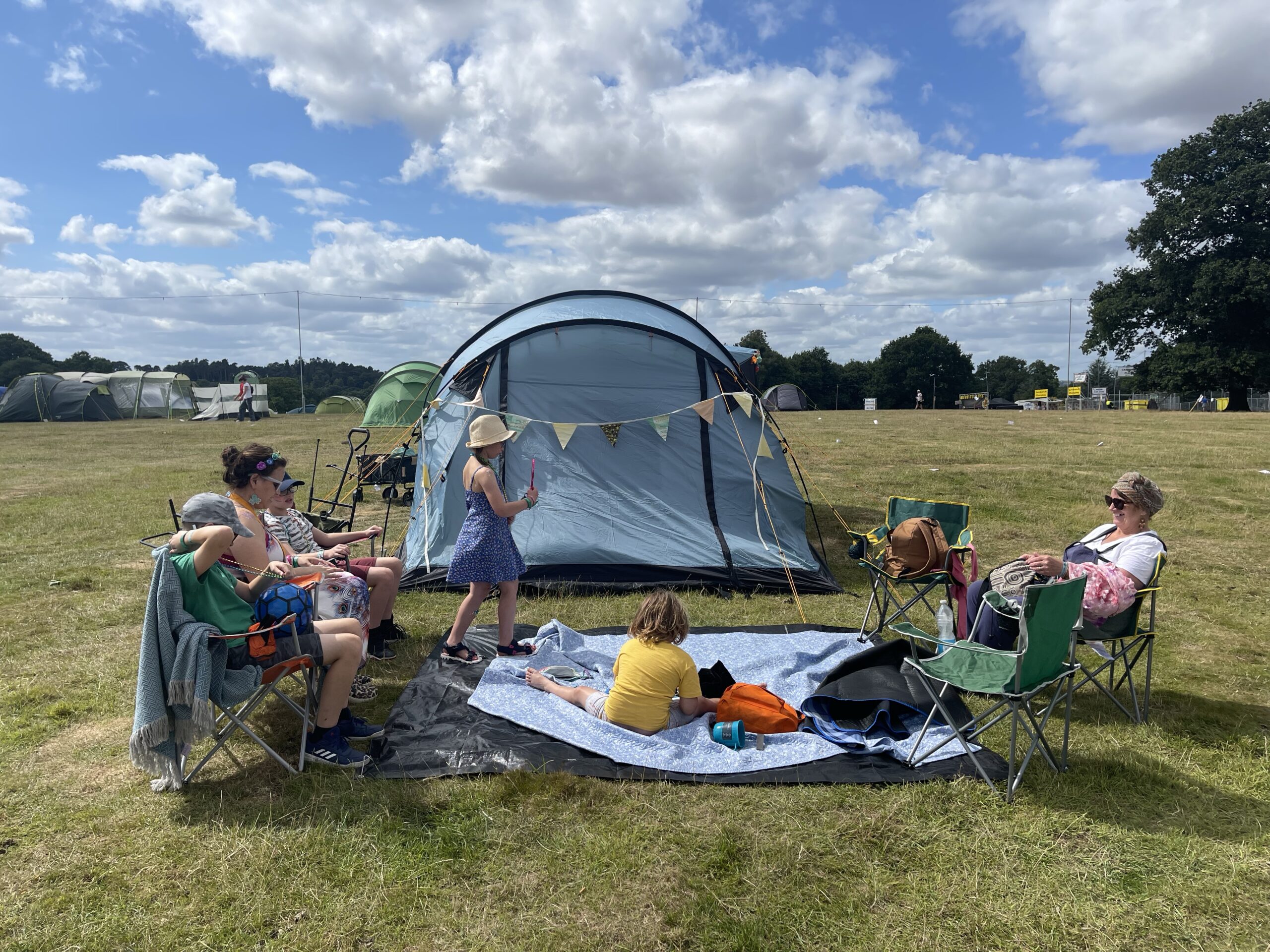 Family enjoys a sunny day outside their tent at a campsite.