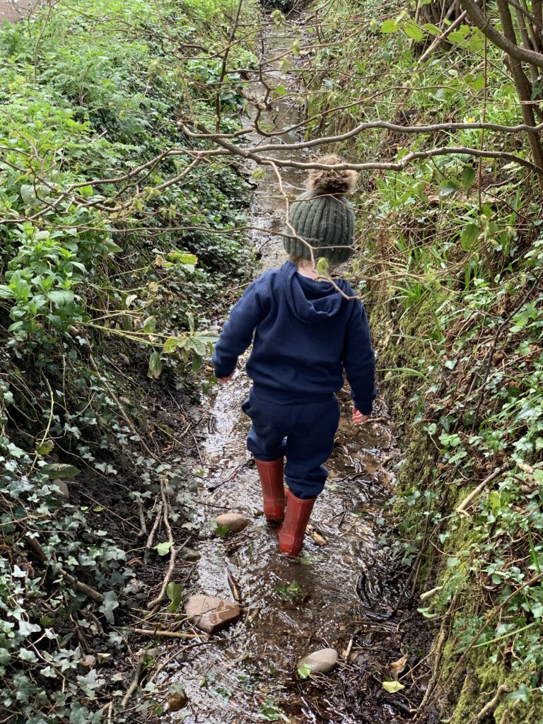 a little boy walking down a muddy path in the woods.