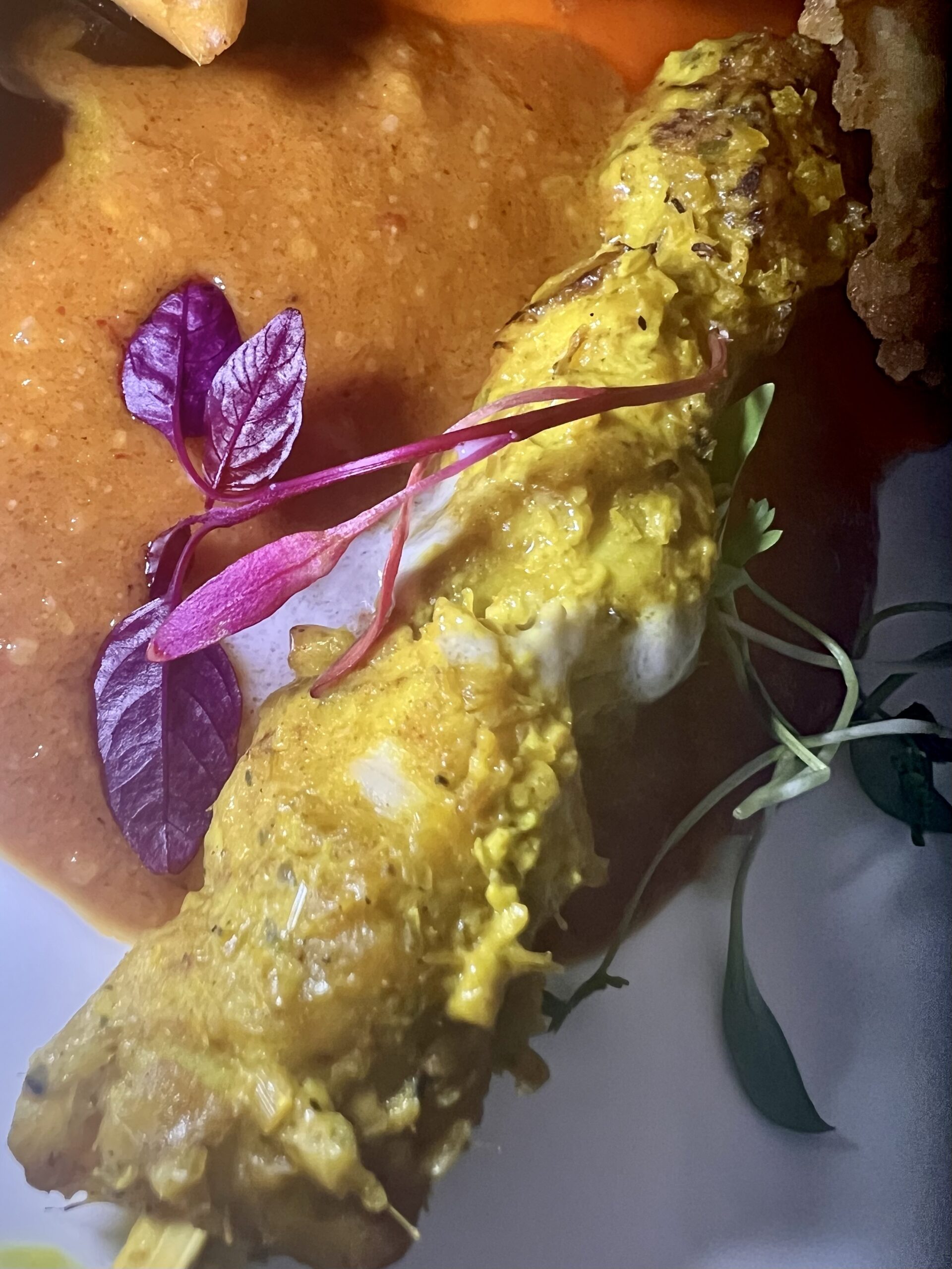 A close-up shows a grilled skewer of yellow marinated meat from Giggling Squid, topped with microgreens and served with a reddish-brown sauce.