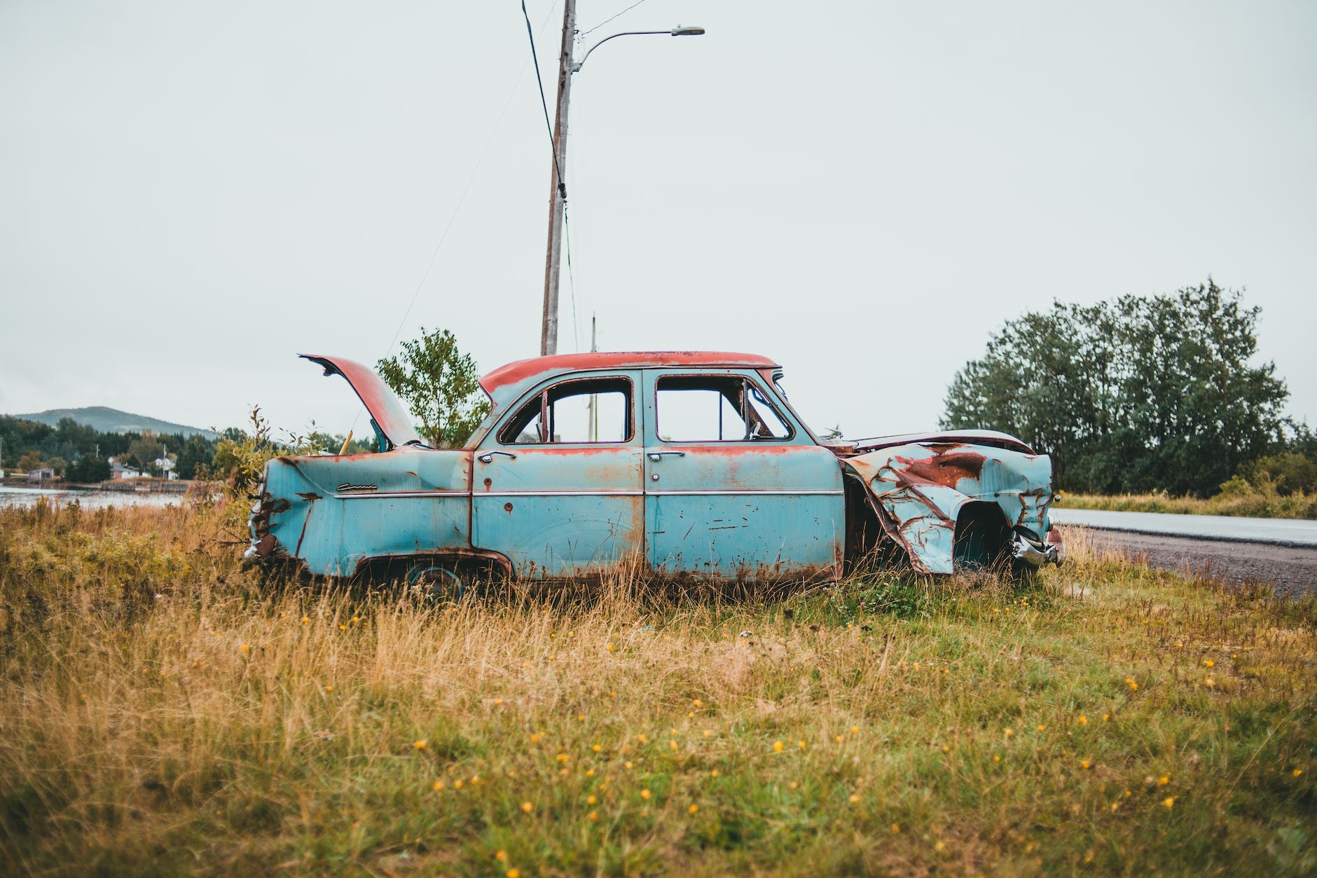 An old rusted car sits on the side of the road.