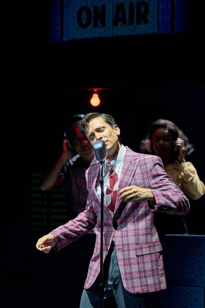 A man in a pink suit singing into a microphone.