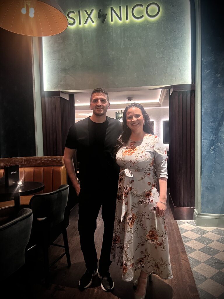 A man and woman standing in front of the six nico restaurant.