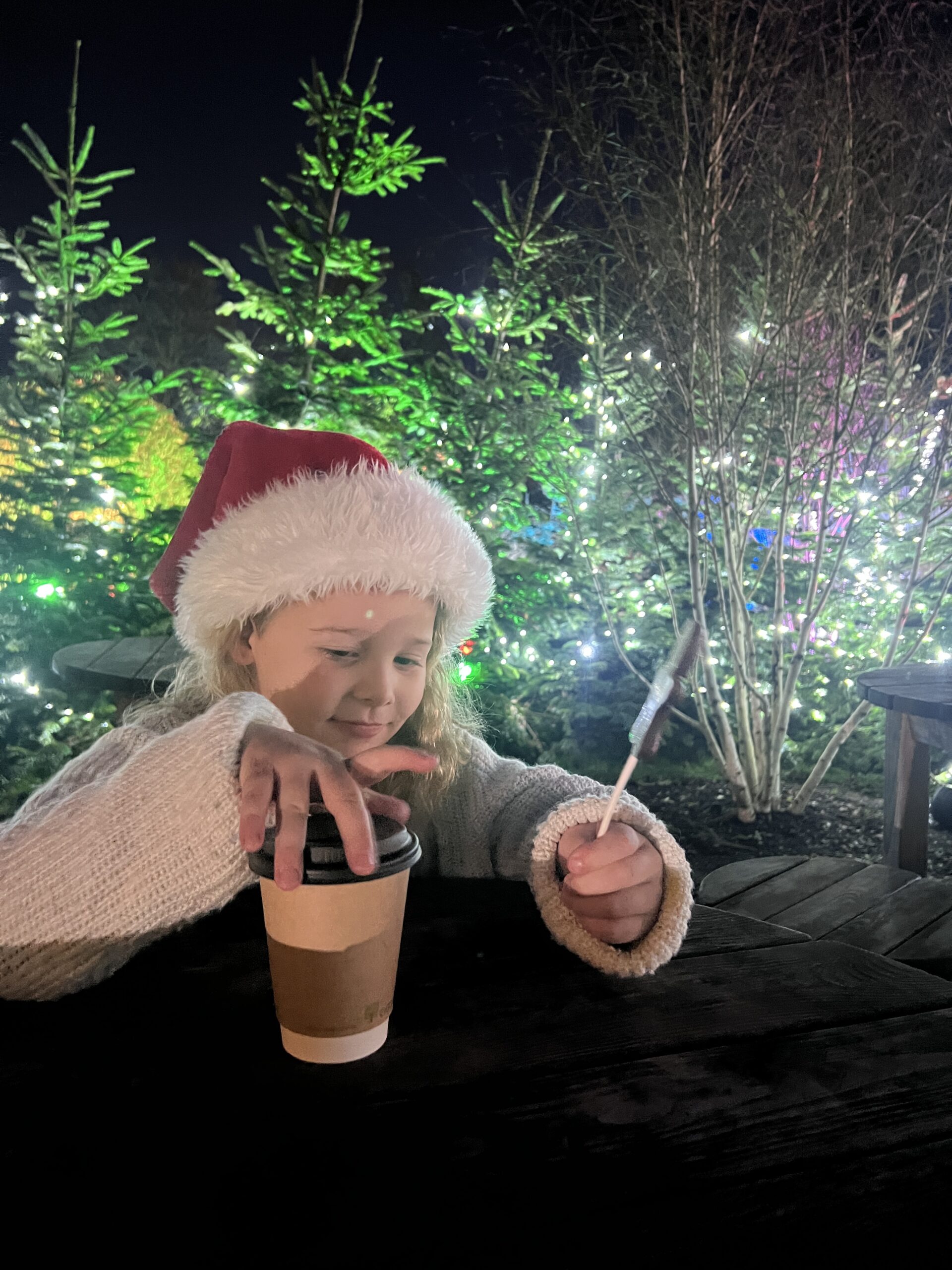 A girl in a santa hat eating a cup of coffee.