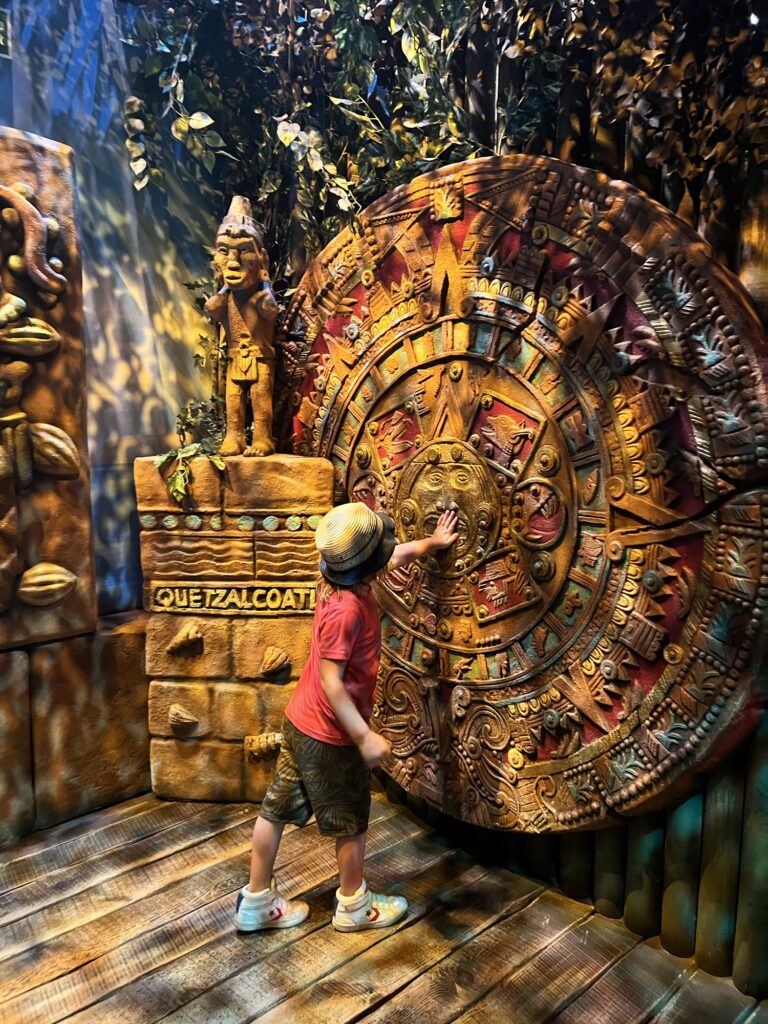 A child is standing in front of a large aztec clock.