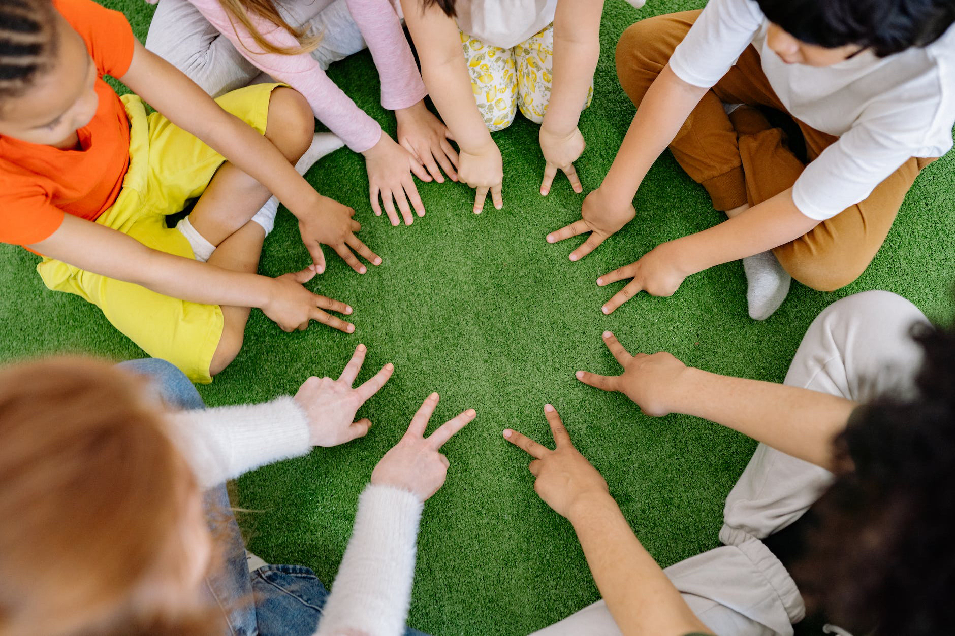 A group of children are sitting around a circle of green grass.