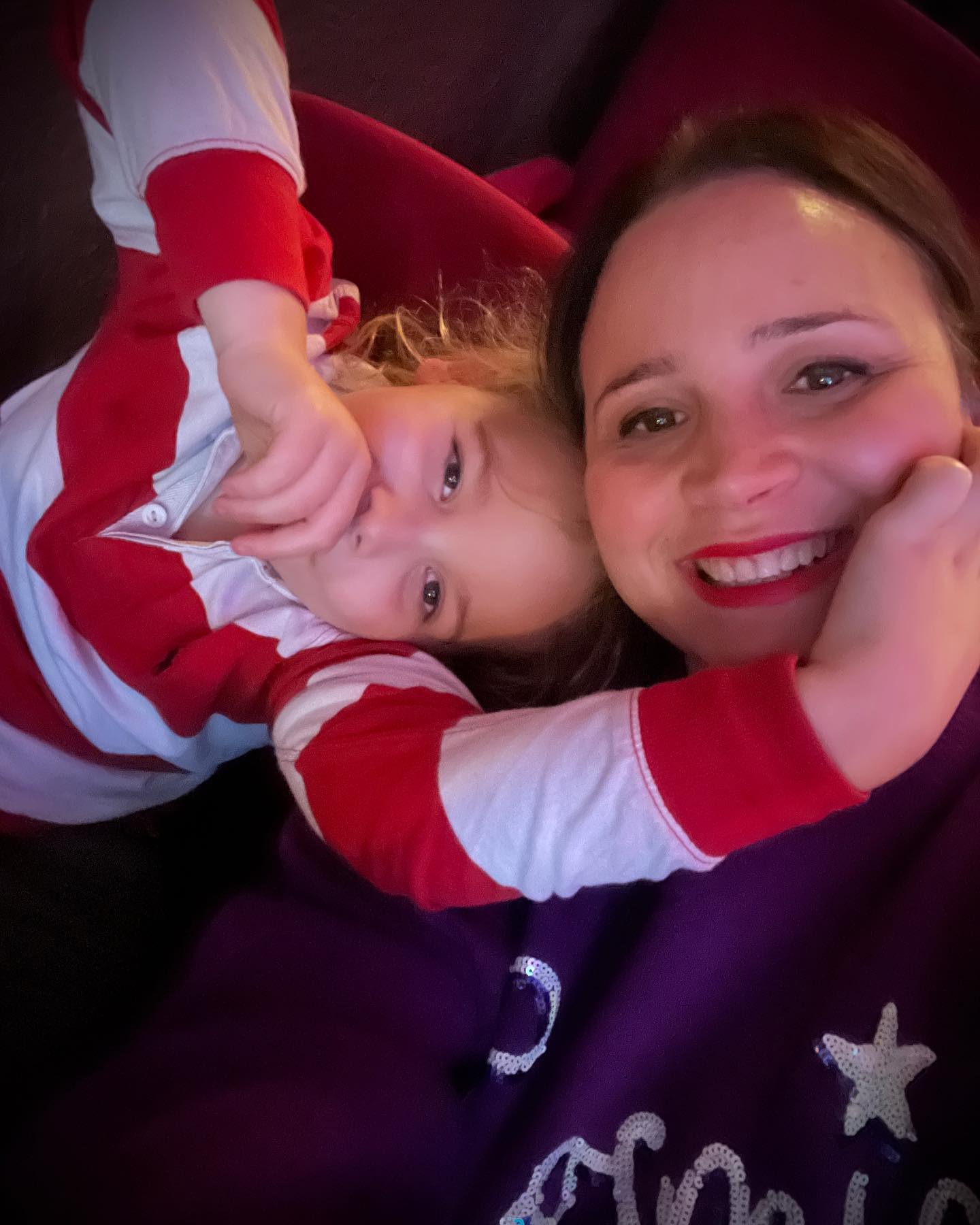 A smiling brummy mummy taking a selfie with a young child resting on a purple blanket.