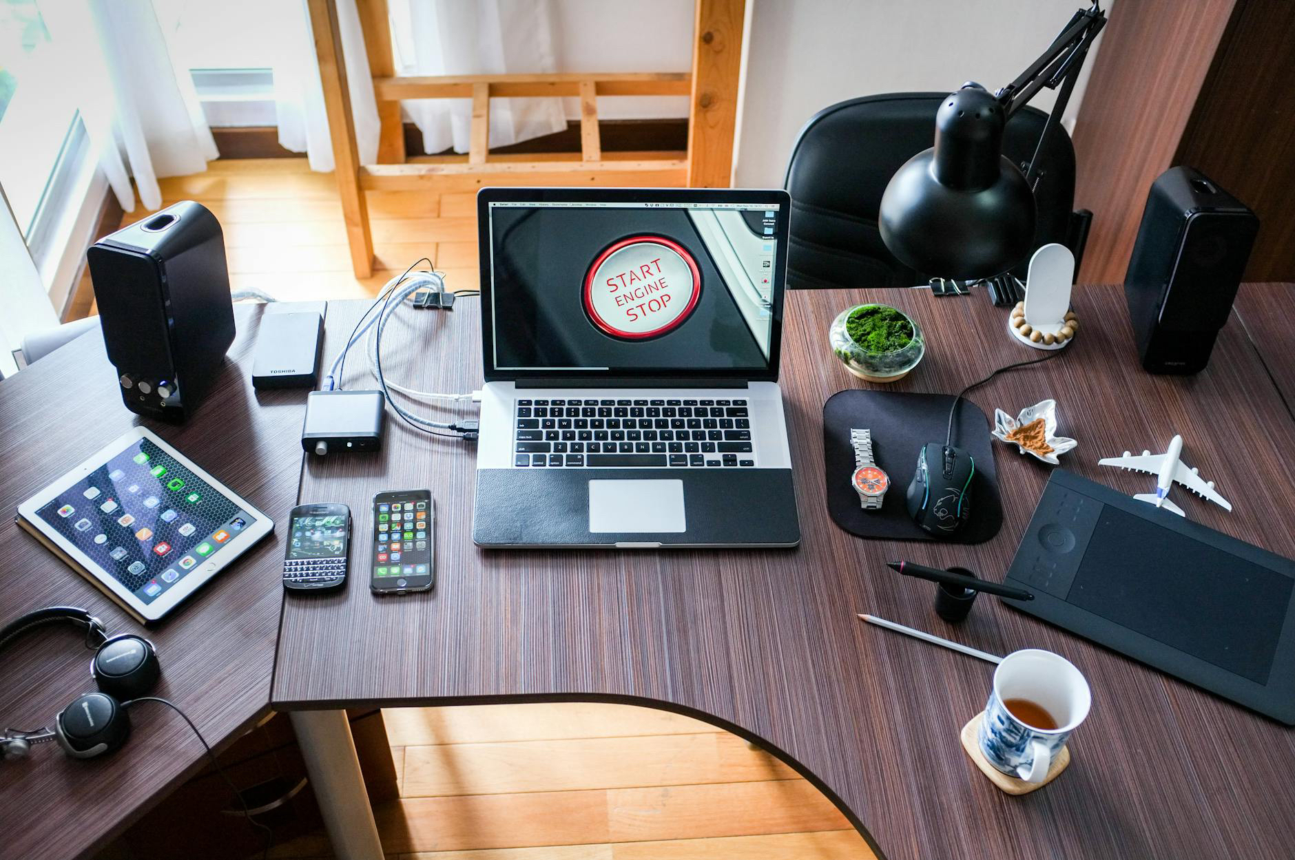 A well-equipped home office setup with multiple tech gadgets and a laptop displaying a 'start/stop' button on the screen.