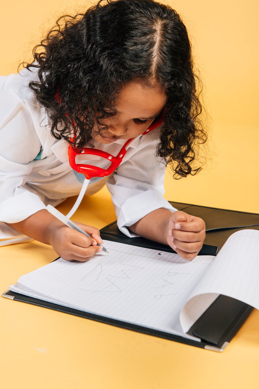 A child in a lab coat with a stethoscope writing in a notebook.