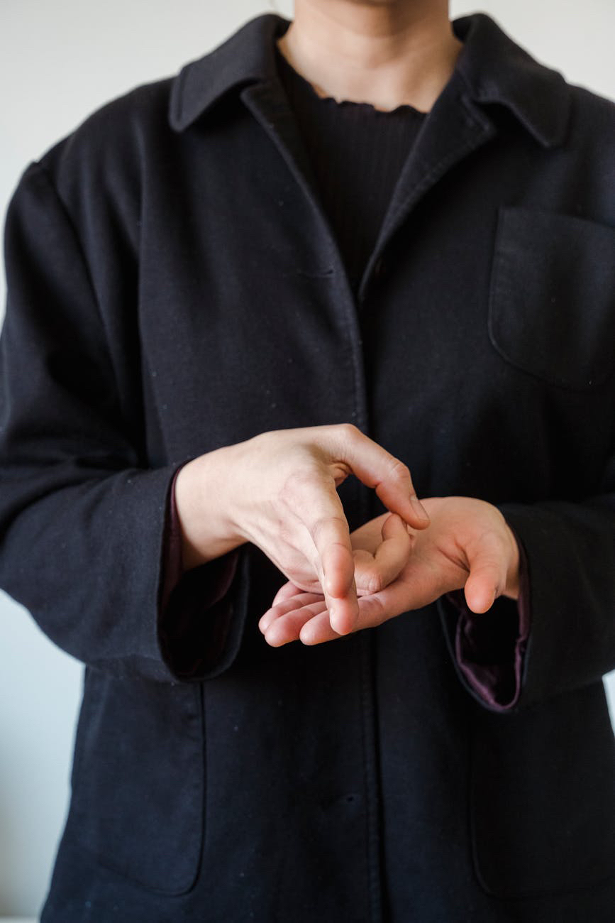 Person in a dark coat performing a hand gesture against a plain background.