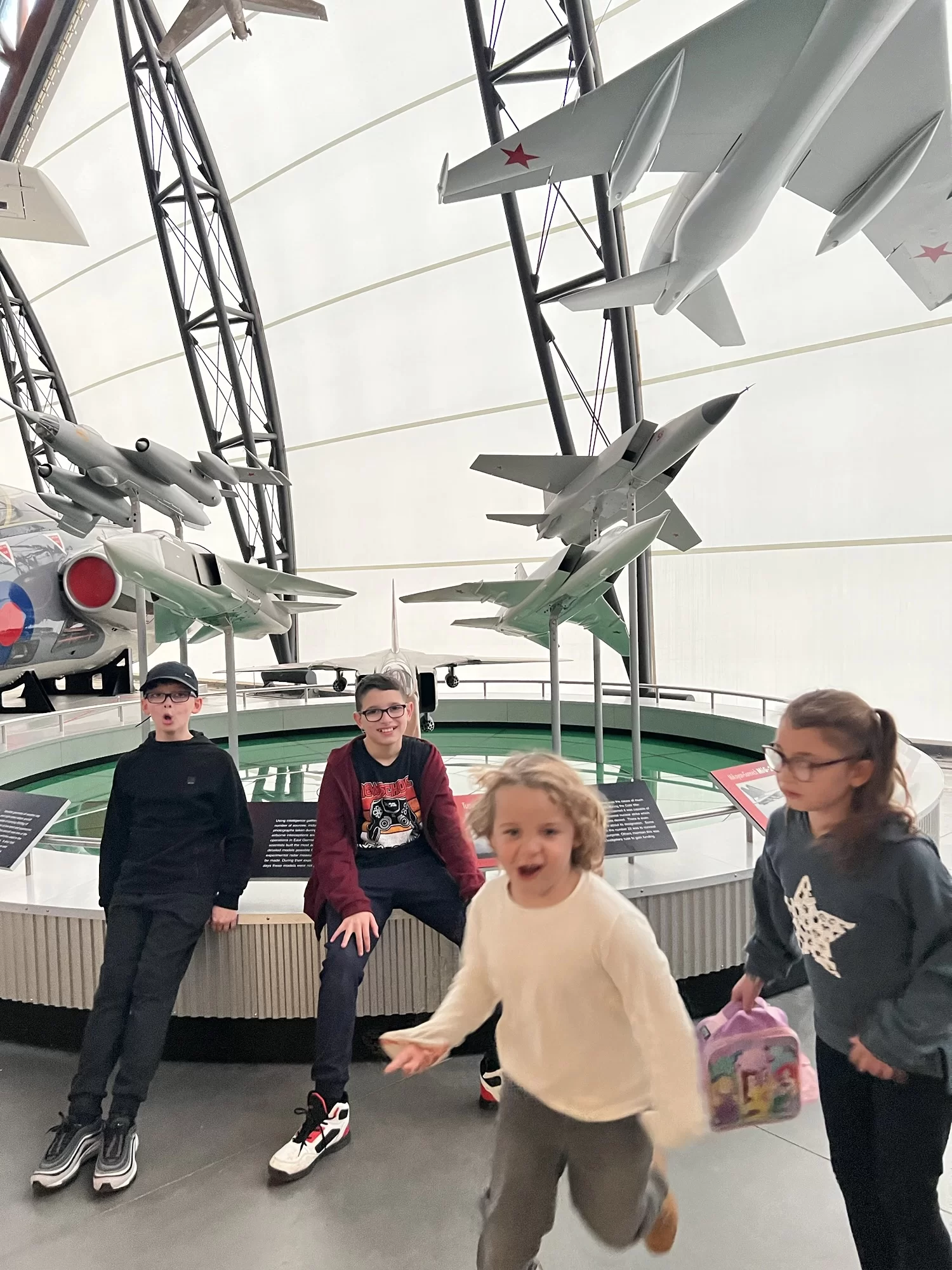 Four children are posing and moving near model aircraft displays inside a museum.