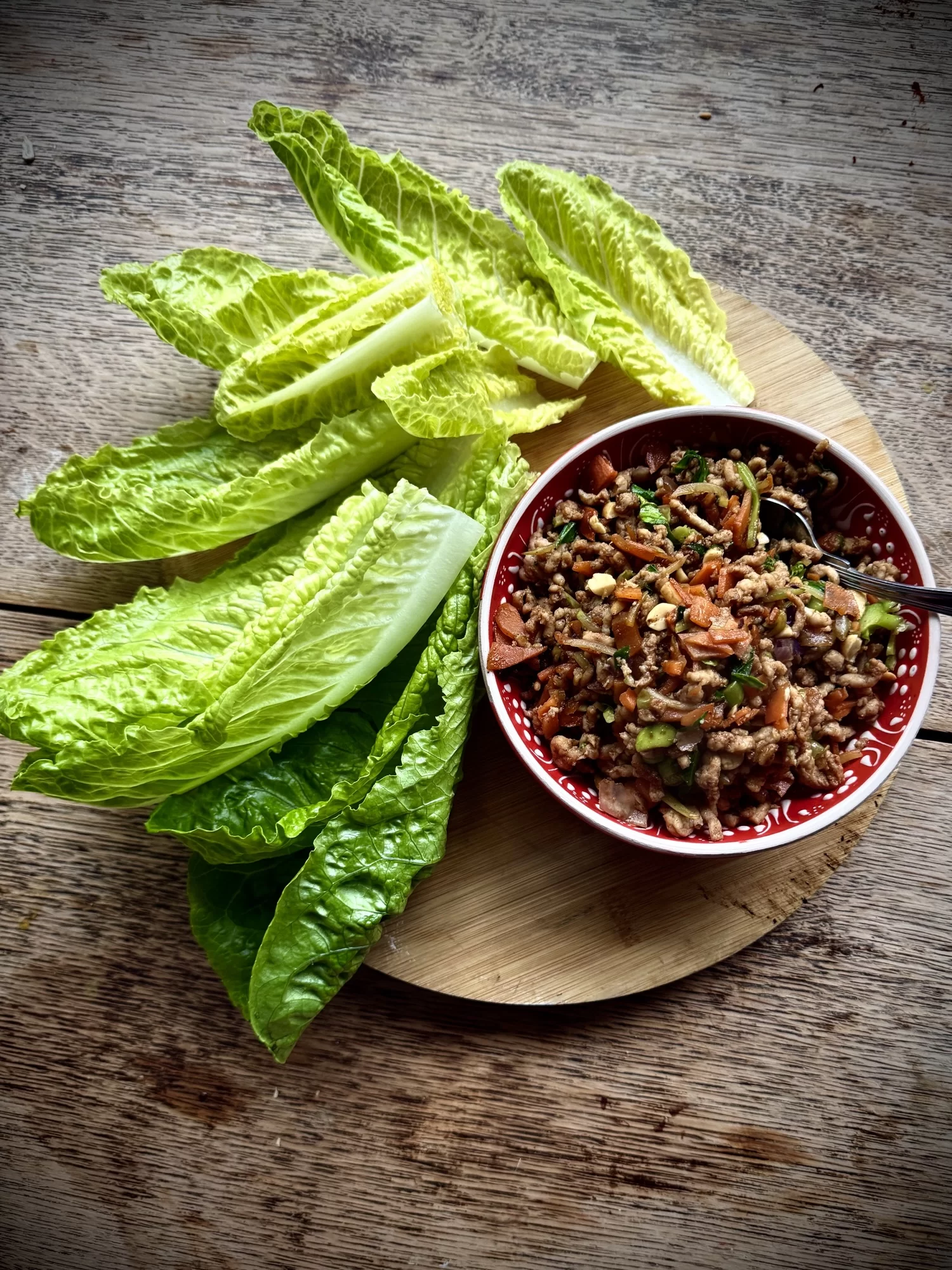 Bowl of minced meat and vegetables with fresh romaine lettuce leaves on a wooden board.
