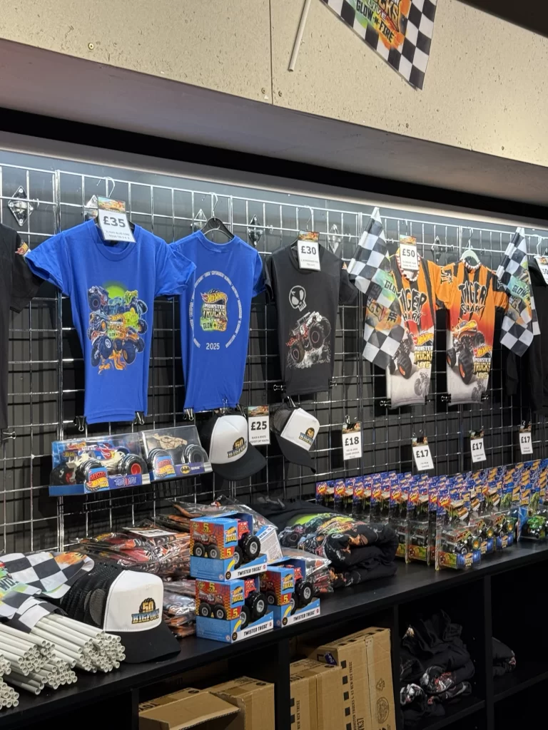 Merchandise display featuring t-shirts, hats, toy cars, and checkered flags with price tags on a wire grid wall.