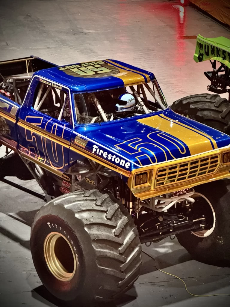 A blue and yellow monster truck with the number 50 on the sides, parked indoors on a concrete floor.