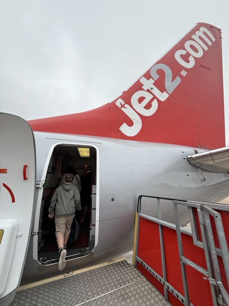 A person boards a Jet2.com airplane via a ramp on a cloudy day, seen near the aircraft's red tail fin.