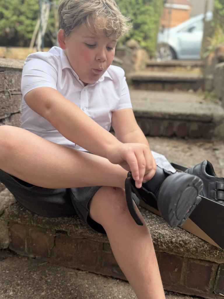 A young boy sits on outdoor steps, focused as he ties his black shoe.