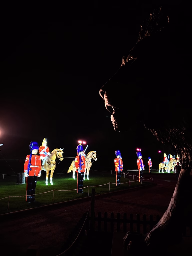 Statues of soldiers and horses are lit up on a dark lawn, with a large animal shape shown in the foreground to the right.