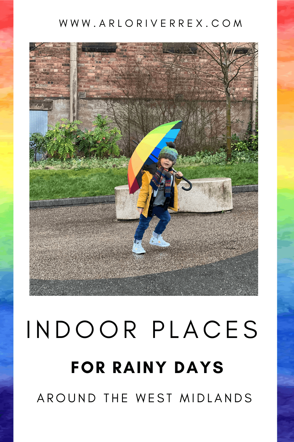 A child in a yellow coat and scarf walks outside with a rainbow umbrella on a rainy day, passing a brick wall and plants.