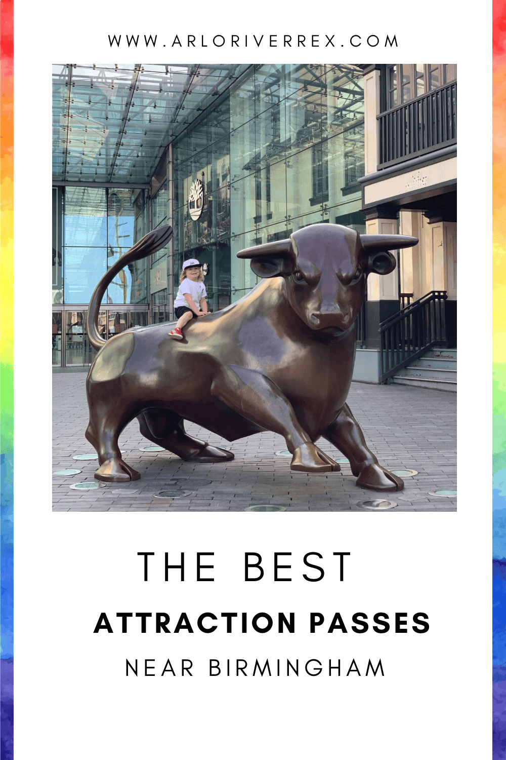 A child sits on a bronze bull statue outside a Birmingham shopping centre, with shops and a glass canopy in the background.
