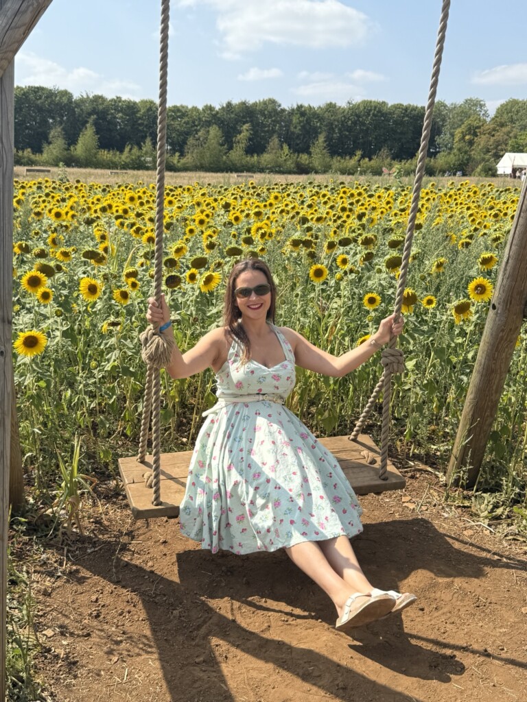 A woman sits on a swing surrounded by blooming sunflowers in a field.
