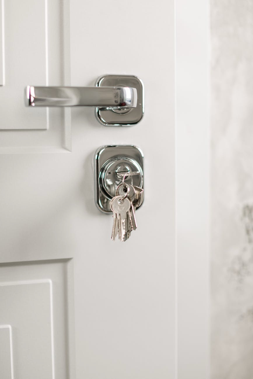 Keys are in the lock of a white door with a silver handle.