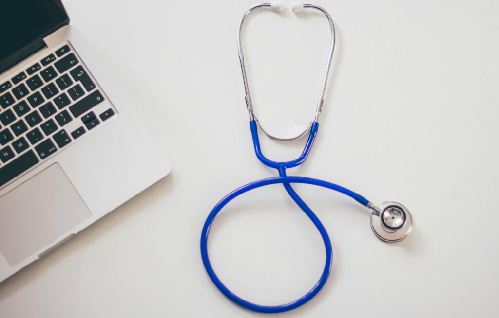 A blue stethoscope rests beside an open laptop on a white table.