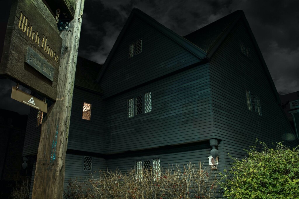 At night, a wooden house with lattice windows is shown, one window lit and a weathered "Witch House" sign in front.
