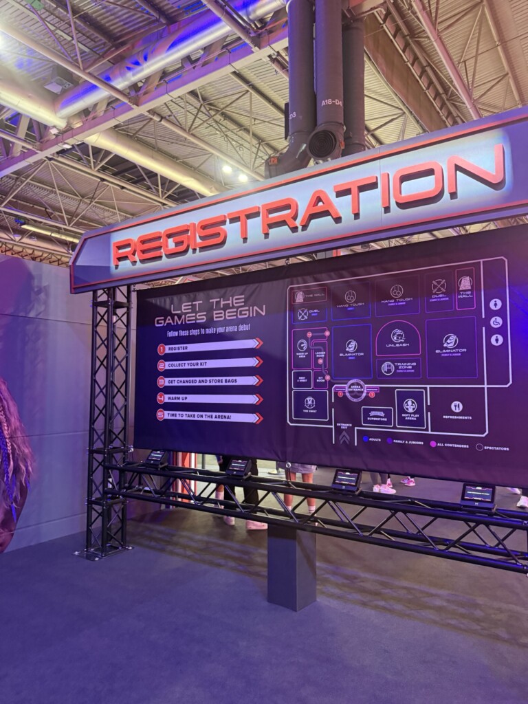 A registration stall at a gaming event with a large sign and an event information board displayed in the background.