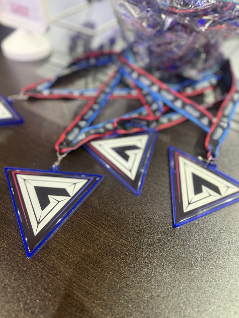 Triangular medals with bright geometric patterns hang from colourful lanyards on a dark table-top.
