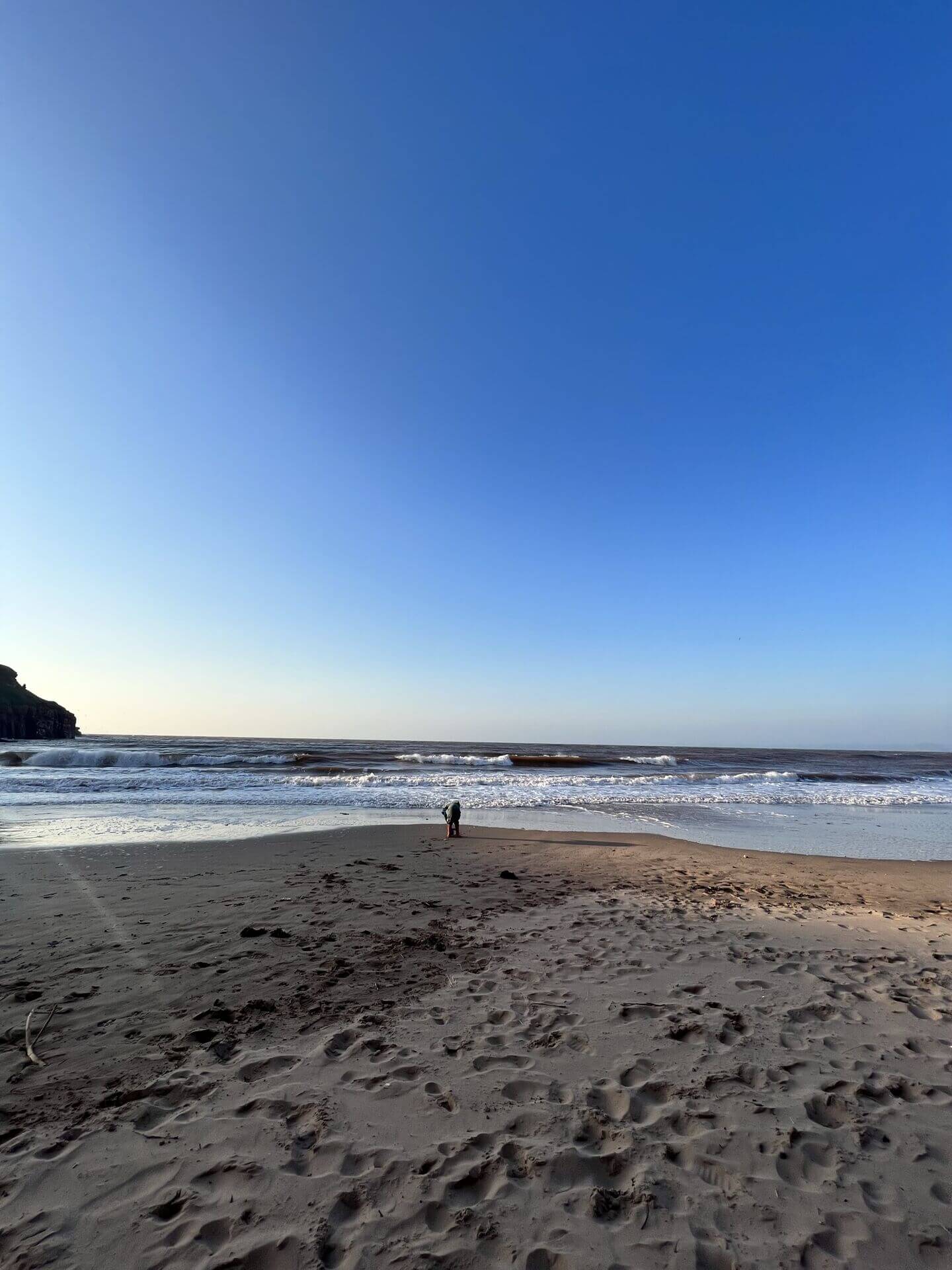 Little boy walking alone on the empty sandy beach near Devon Cliffs Haven at low tide